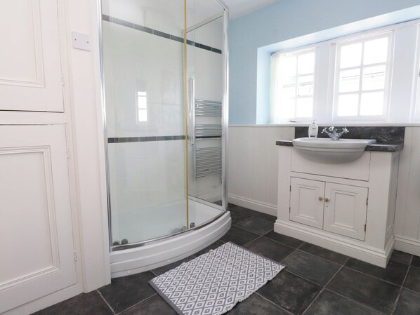 Une salle de bain dotée d’une douche à parois de verre, de meubles blancs, d’un lavabo avec un plan de travail en marbre et d’un tapis à motifs.