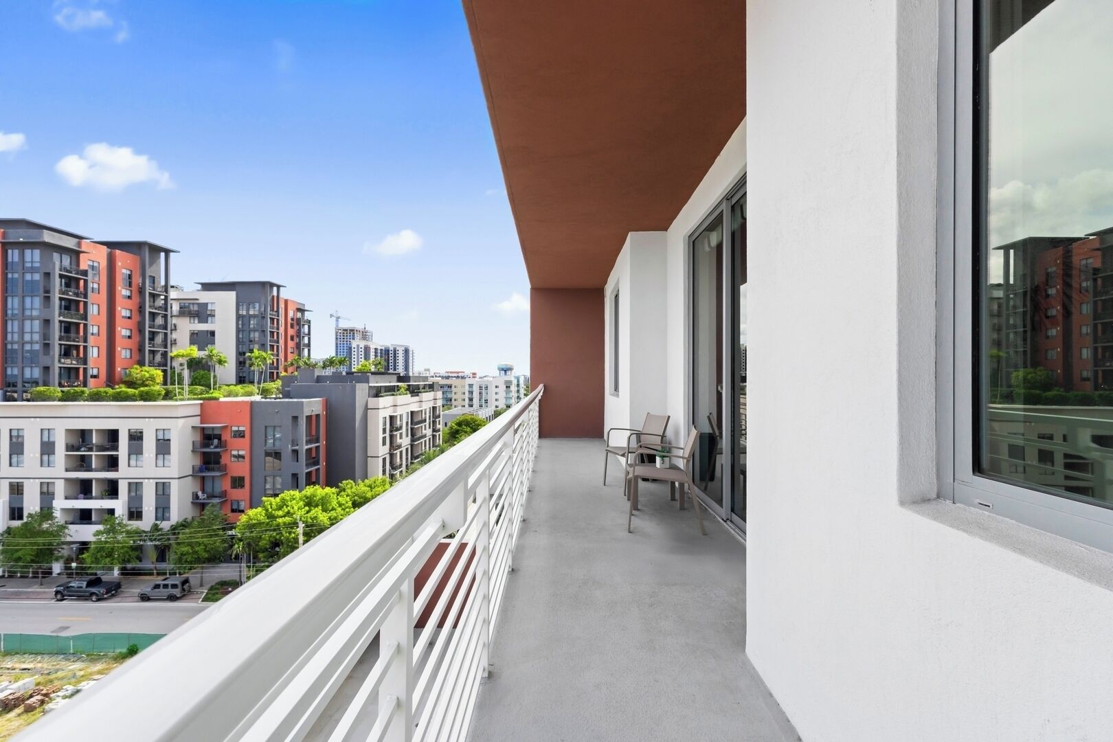 A balcony with a view of modern buildings, a white railing, and a table with chairs.
