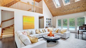 Een ruime woonkamer met een hoge plafond, een groot raam en een trap naar een hoger niveau.
