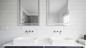 Une salle de bain avec deux lavabos blancs, un grand miroir et une douche.