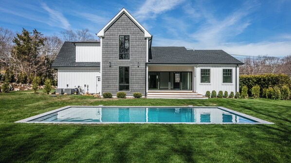 Une maison moderne à deux étages, dotée d’une grande pelouse à l’avant et d’une piscine rectangulaire.