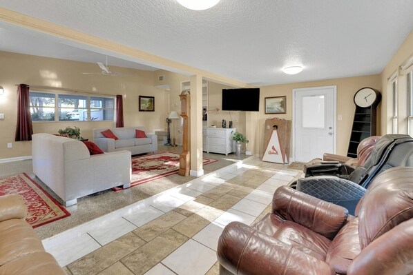 A spacious living room with a white sofa, a red and beige rug, a brown leather couch, and a flat-screen TV mounted on the wall.