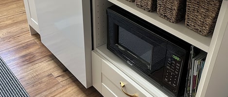 A compact kitchen with a built-in microwave, a dishwasher, and wicker baskets on the countertop.