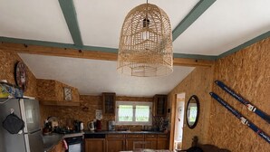 A kitchen with wooden cabinets, a dining table set for four, and a hanging light fixture. - Nature chalet on 8000m2 of totally quiet land in Coinchimont (Ban-de-Laveline)