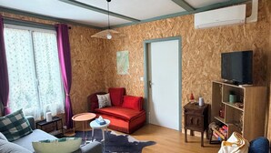 A living room with a sofa, a red couch, a TV stand, and a wooden floor. - Nature chalet on 8000m2 of totally quiet land in Coinchimont (Ban-de-Laveline)
