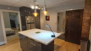 Een moderne keuken met een centraal eiland, een roestvrijstalen koelkast, hanglampen en een deur naar een andere kamer.