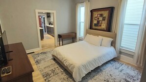 Een slaapkamer met een bed, een bureau, een stoel, een vloerkleed en een fotolijst aan de muur.