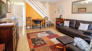 A living room with a brown leather sofa, a wooden dining table with chairs, a patterned rug, and a staircase leading to another room. - Sweetacres (Great Yarmouth)