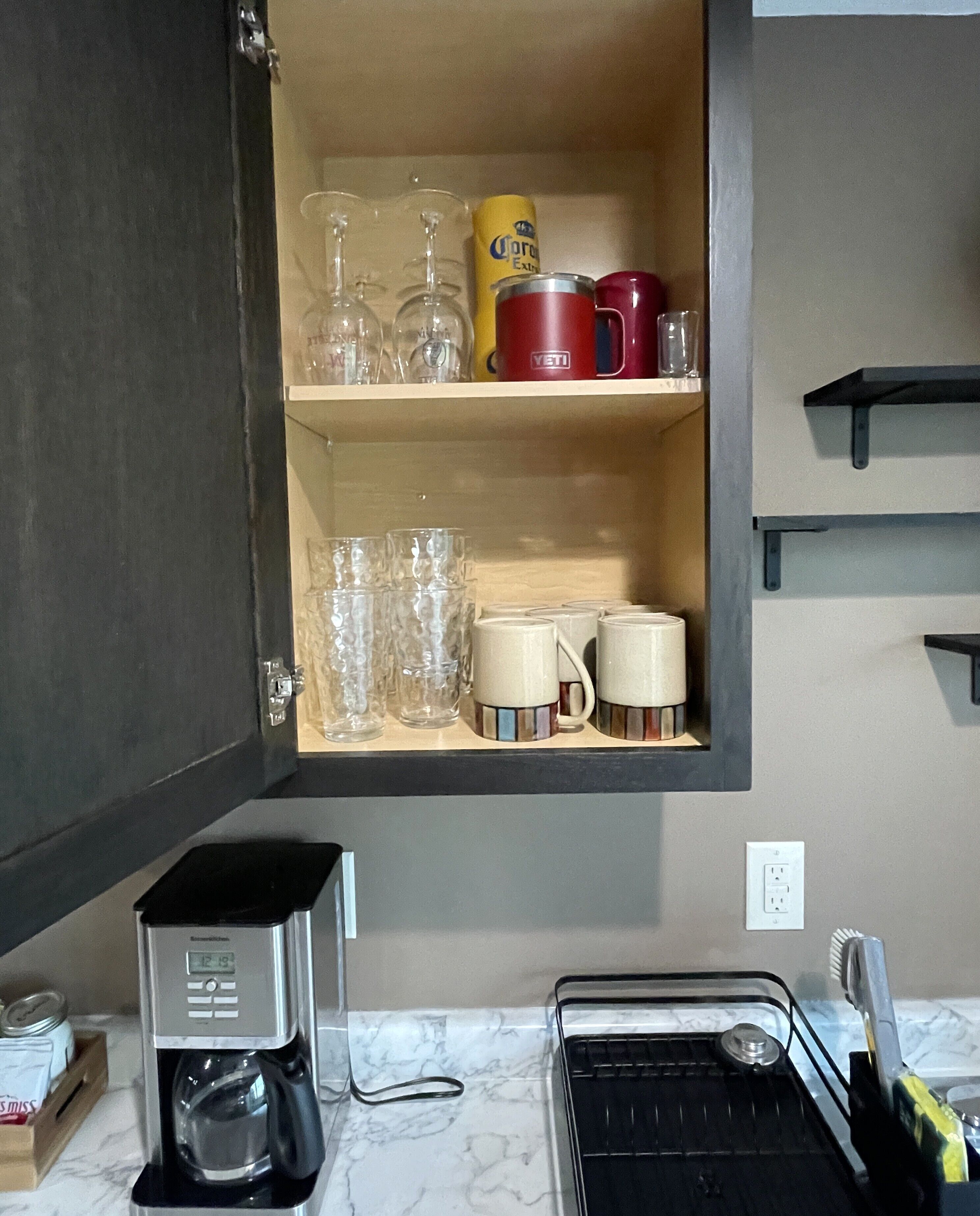 Una cocina con cafetera, pileta y estantes con vasos y tazas.