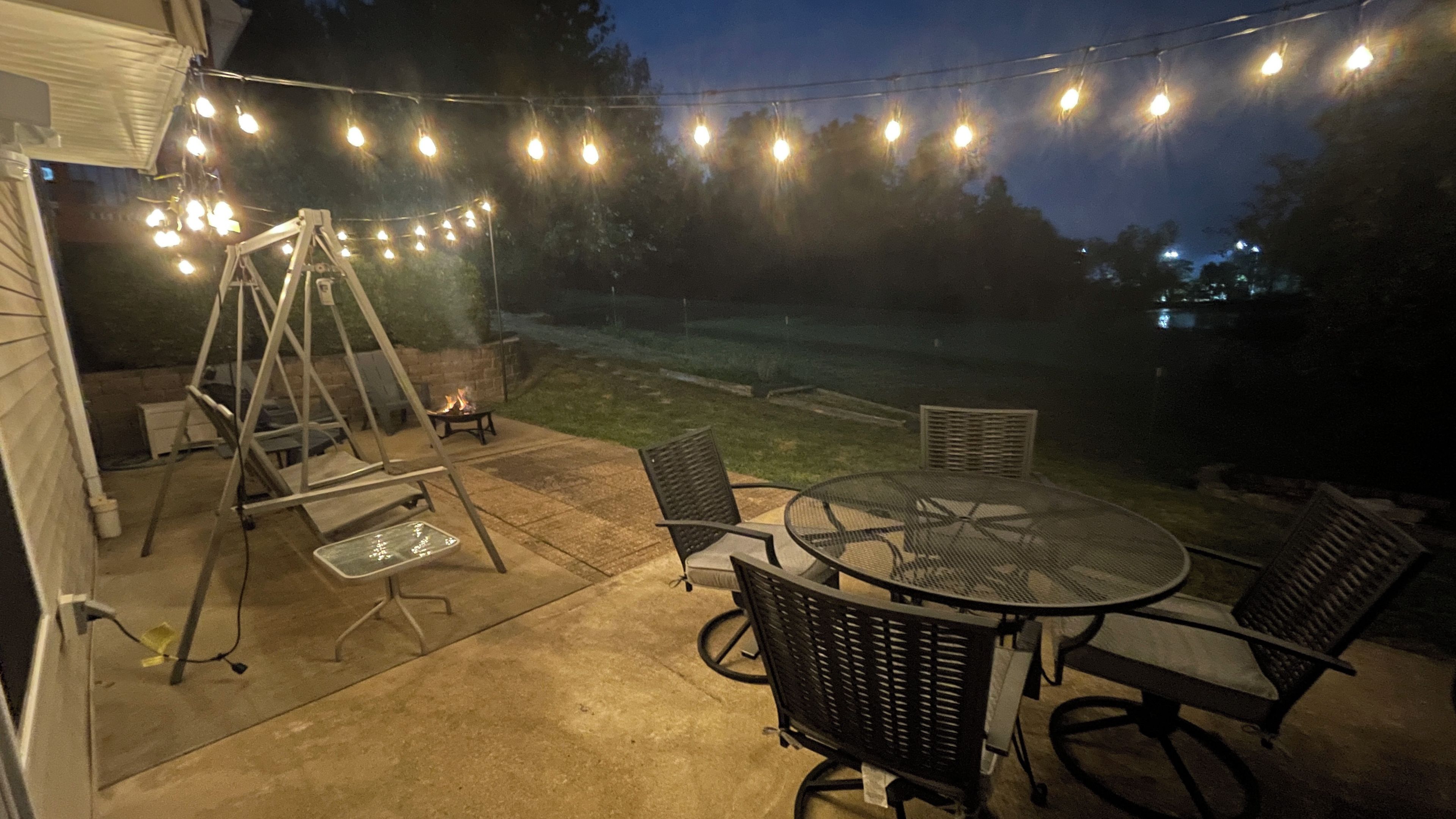 Ein Außenbereich mit einer Terrasse, einer Schaukel, einem Tisch mit Stühlen und Lichterketten.