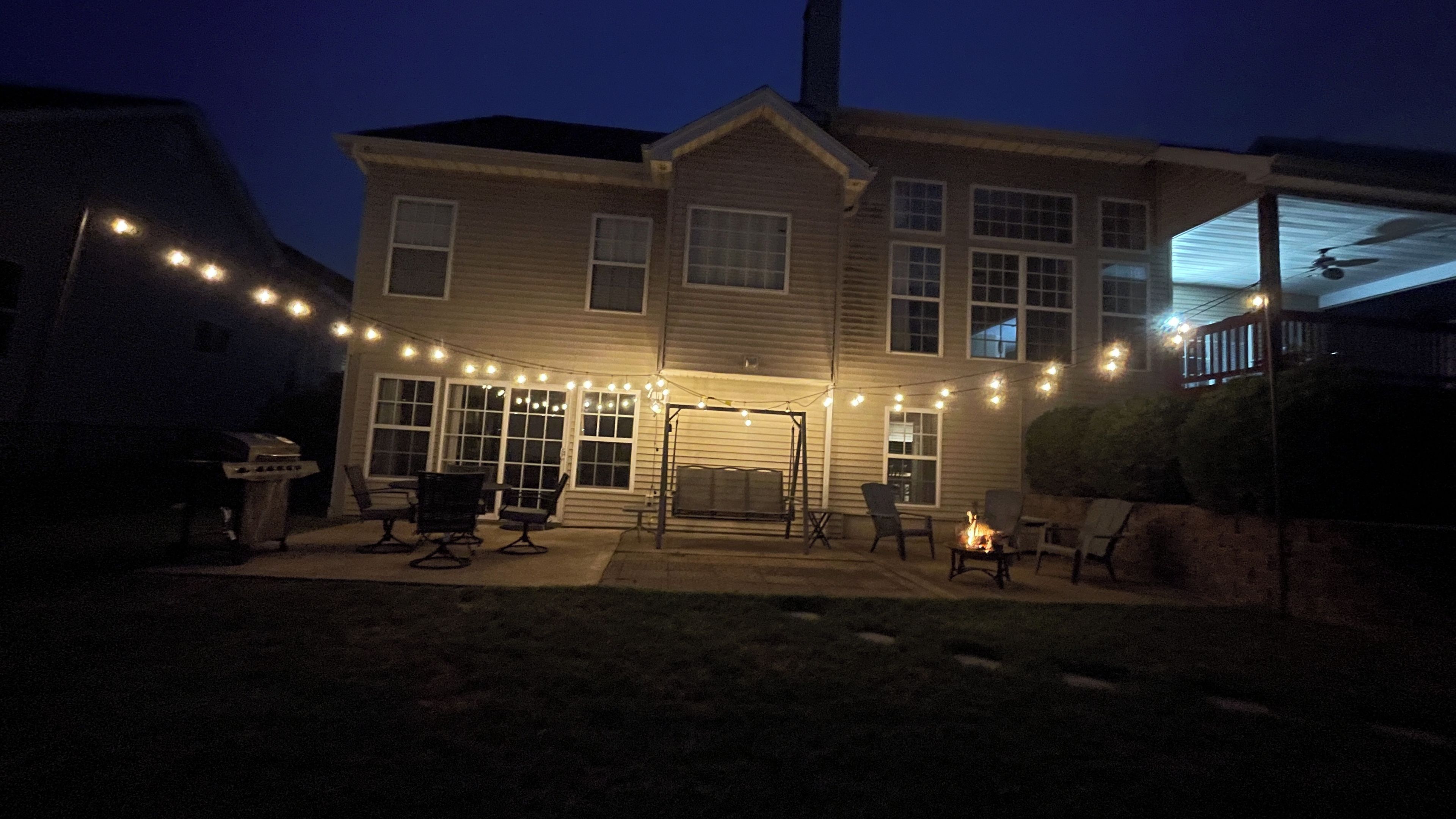 A two-story house with a covered patio area, string lights, and outdoor furniture.
