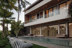 Una casa moderna de dos pisos con piscina, mobiliario exterior y abundante vegetación.