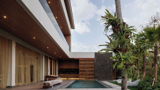Un edificio moderno con piscina, asientos al aire libre y plantas tropicales.