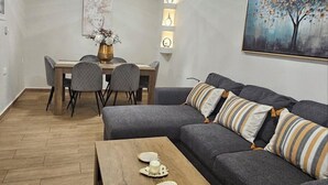 A modern living room with a sectional sofa, a wooden coffee table, a dining table with chairs, and a painting on the wall. - Casa Di Mare Artemis,near airport,near sea (Artemis)