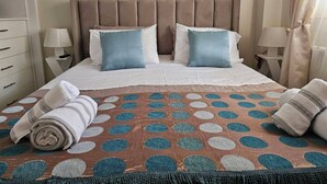 A neatly made bed with a polka dot bedspread, two pillows, and rolled towels on a hotel room with a simple headboard and bedside tables. - Casa Di Mare Artemis,near airport,near sea (Artemis)