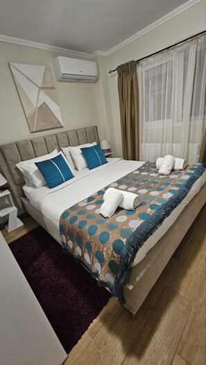 Hotelkamer met een bed, hoofdeinde, raam met gordijnen, een wandairconditioner en een klein tafeltje met een stoel.