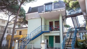 A two-story building with a green door, a balcony on the upper floor, and a blue staircase. - Charming 2-room Apartment in a Peaceful Residential Area (Rosolina)