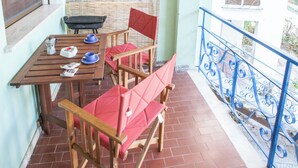A balcony with a wooden table, two chairs, and a window with a bamboo blind. - Charming 2-room Apartment in a Peaceful Residential Area (Rosolina)