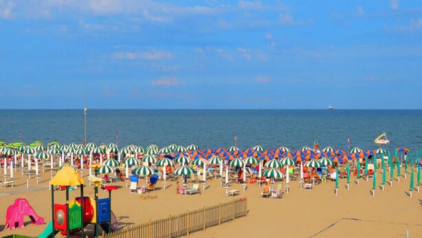 A beach with rows of umbrellas and beach chairs, a playground, and a fence. - Charming 2-room Apartment in a Peaceful Residential Area (Rosolina)