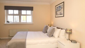 Une chambre à coucher avec un lit, des lampes de chevet, un radiateur, une fenêtre avec des stores et un tableau encadré au mur.