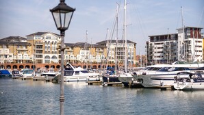 Un port de plaisance avec des bateaux amarrés, un lampadaire au premier plan et des immeubles à plusieurs étages en arrière-plan.