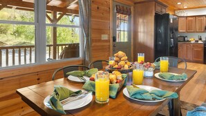 Une table de salle à manger en bois, avec des aliments pour le petit-déjeuner, une vue sur l’extérieur et un coin cuisine.