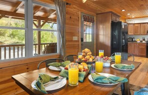 A wooden dining table with breakfast items, a view of the outdoors, and a kitchen area. - 2-Homes at Smoky Mountain with Breathtaking Views (Waynesville)