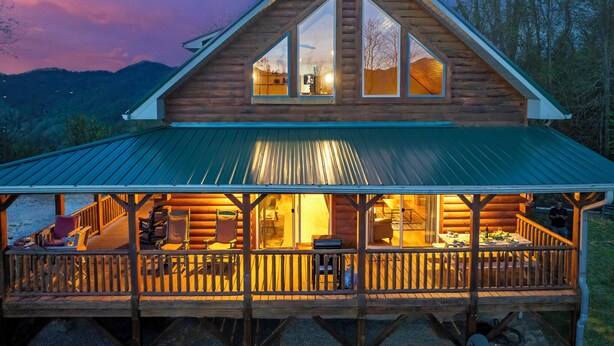 A log cabin with a covered porch, large windows, and a view of the surrounding landscape. - Mountaintop Cabin with Panoramic Views, Fire Pit (Waynesville)