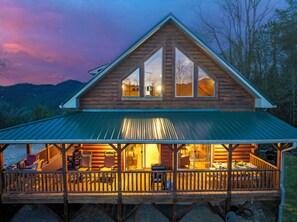 A log cabin with a covered porch, large windows, and a view of the surrounding landscape. - Mountaintop Cabin with Panoramic Views, Fire Pit (Waynesville)