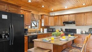 A kitchen with wooden cabinets, a black refrigerator, a microwave, and a dining area with a bench and chairs. - Mountaintop Cabin with Panoramic Views, Fire Pit (Waynesville)
