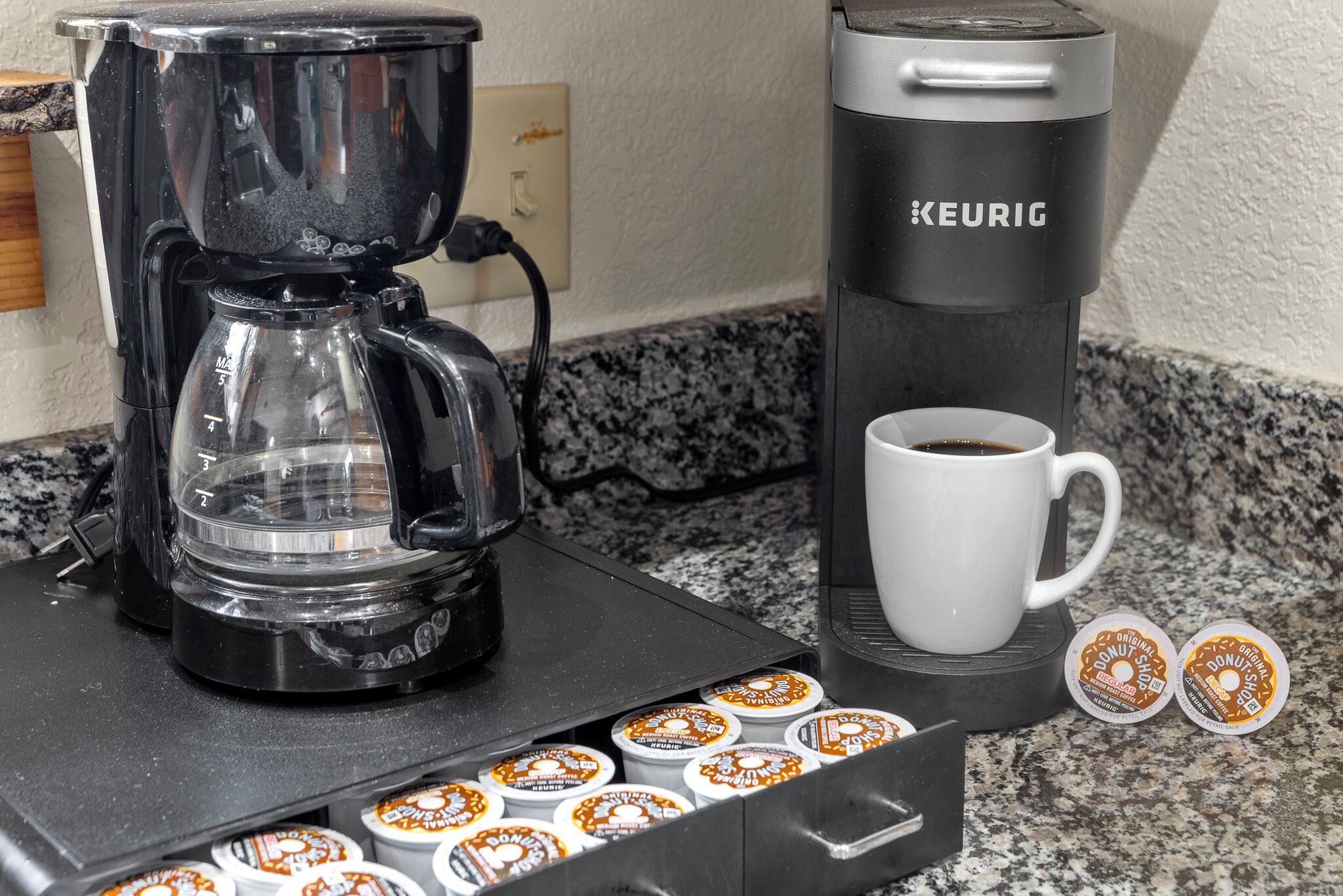 Une machine à café Keurig, une tasse à café et un support à dosettes contenant des dosettes de café, le tout posé sur un comptoir de cuisine.