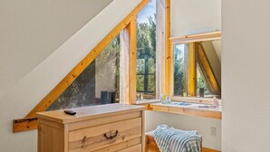 Une chambre avec un plafond en pente, une commode en bois, une fenêtre donnant sur les arbres et une pancarte sur laquelle on peut lire « TRANQUILLITÉ ».