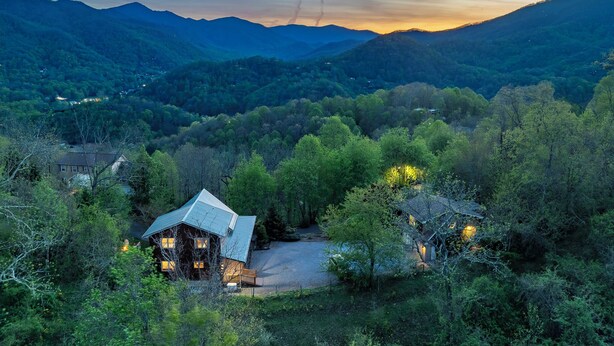Une cabane surmontée d’un toit en métal, entourée d’une forêt dense et de montagnes.
