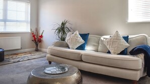 A living room with a beige sofa, a round coffee table, and a potted plant. - 2 bedroom accommodation in Whitby (Whitby)