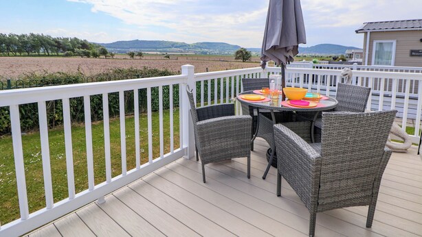 Una terraza con sillas de mimbre y una mesa dispuesta para comer, con vistas a un paisaje rural.