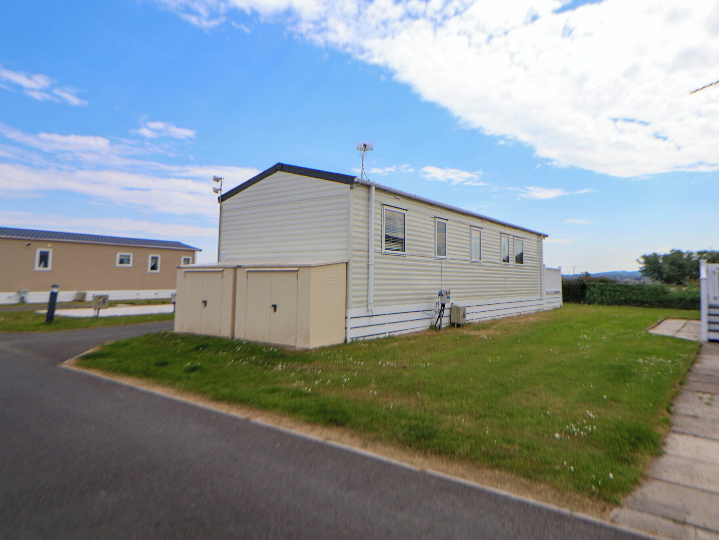 A single-story mobile home with a flat roof, a small attached garage, and a paved driveway.