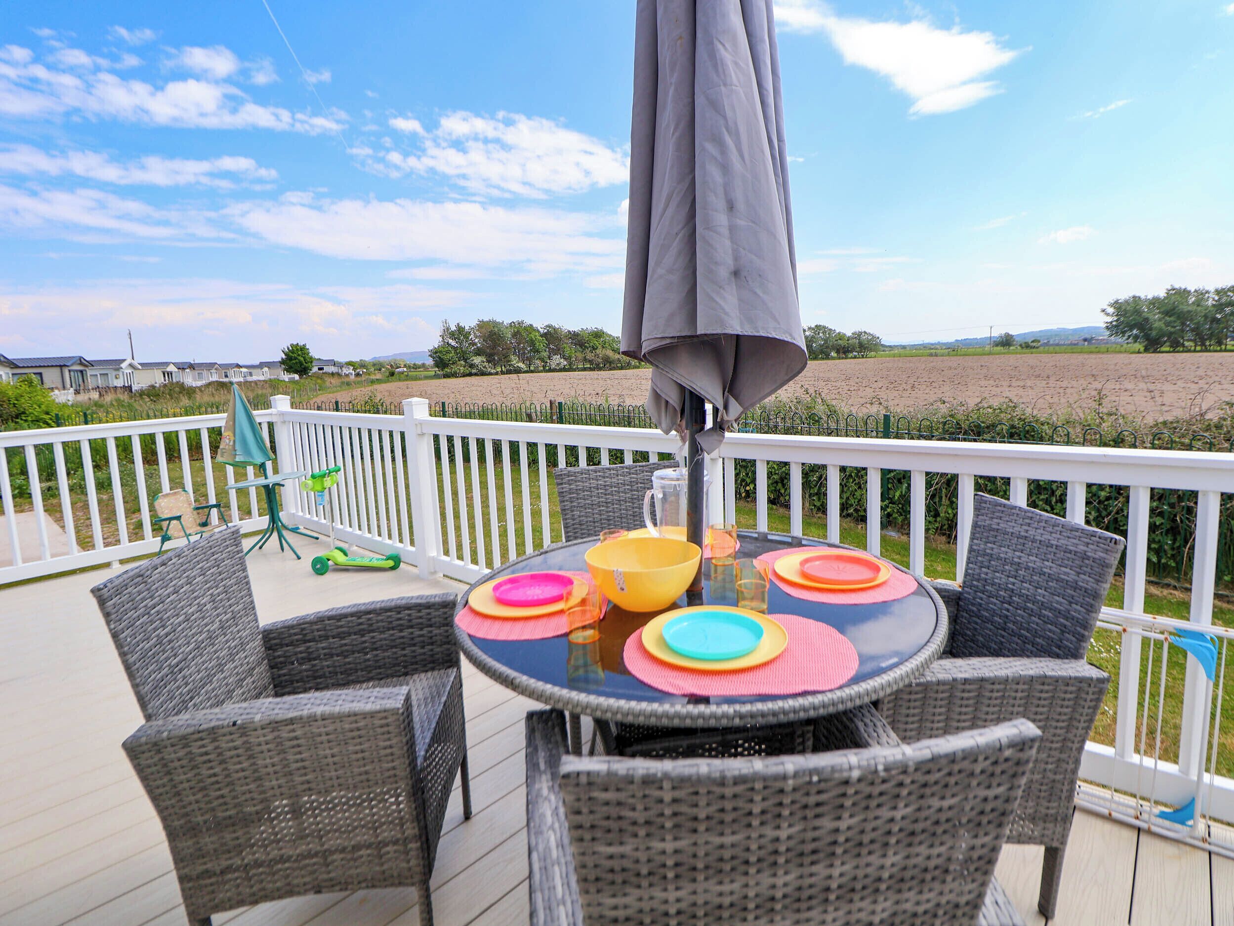 A deck with wicker chairs and a table set with colorful plates, a table umbrella, and a green scooter.