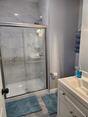 Um banheiro com box de vidro, pia branca e tapete azul.