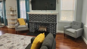 Ein Wohnzimmer mit Kamin, einem flachbildfernseher darüber und zwei Sesseln.