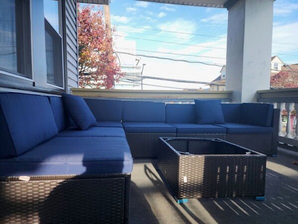 Uma área de estar coberta ao ar livre com um amplo sofá modular e uma mesa de centro de vime.