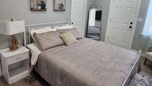 Ein Schlafzimmer mit Bett, Nachttisch und Kommode. Zwei Türen und ein Spiegel sind an der Wand.