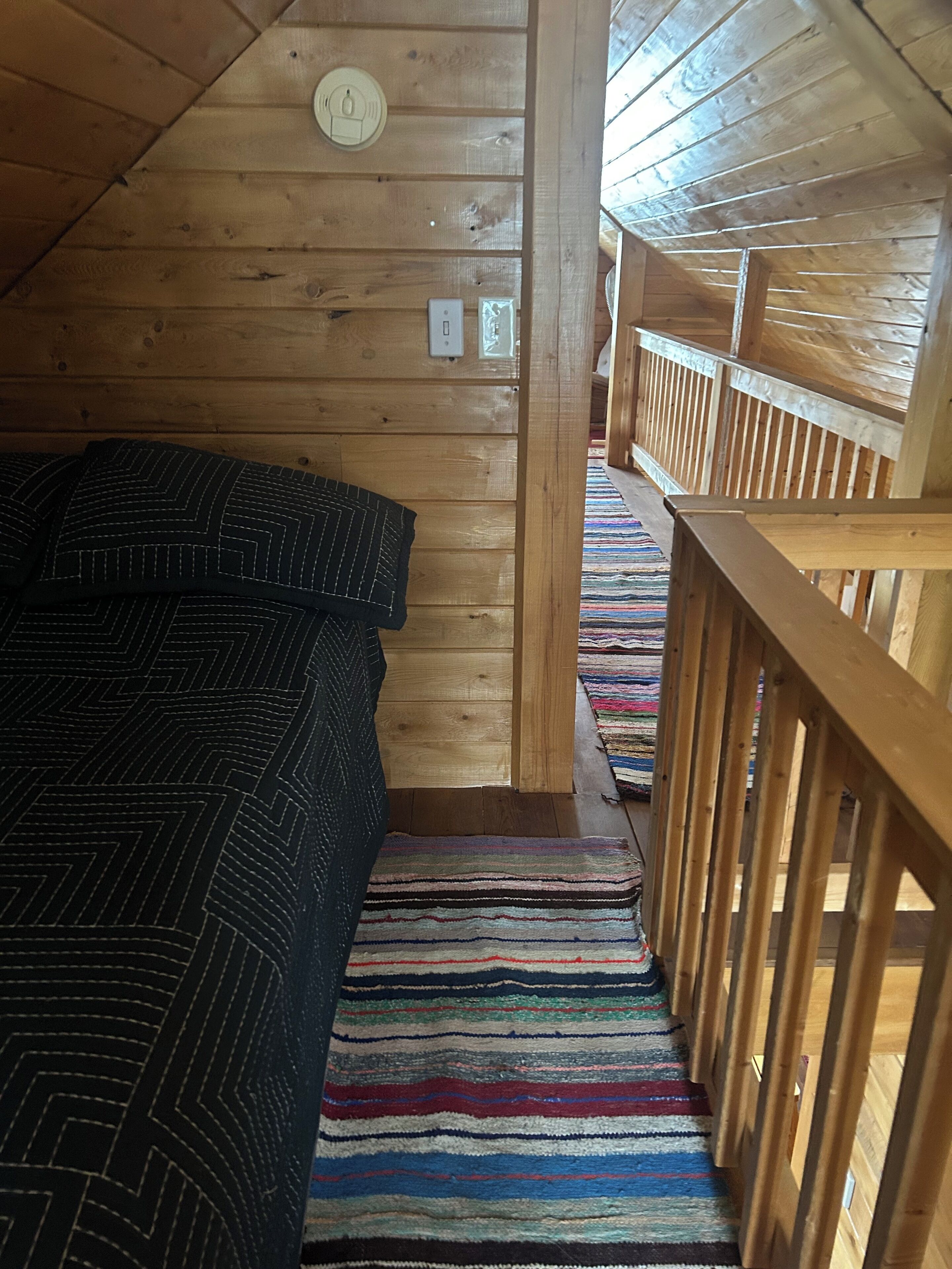 Interior de una cabaña de madera con una cama, una escalera y una barandilla.
