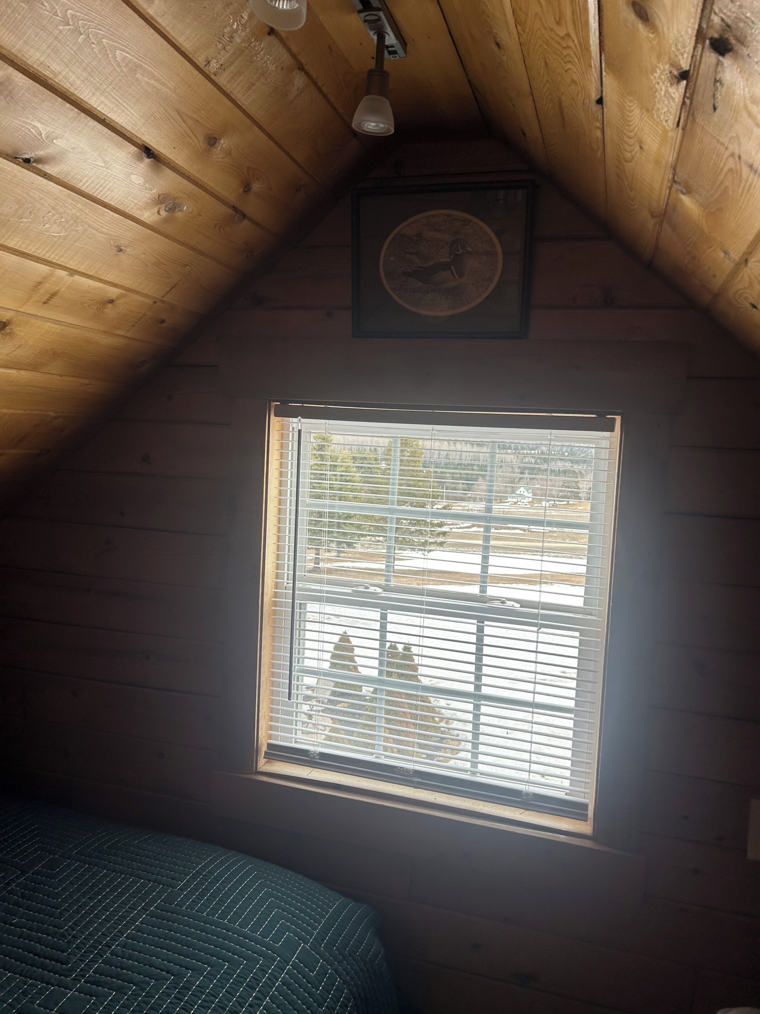 A room with wooden walls, a window with blinds, a bed, and a wall clock.