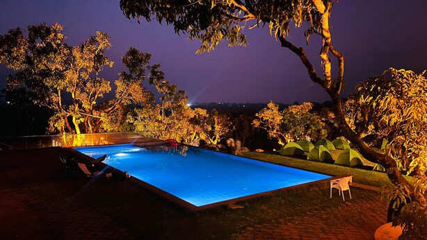 Une piscine extérieure, éclairée la nuit, entourée d’arbres et offrant une vue dégagée sur le ciel.