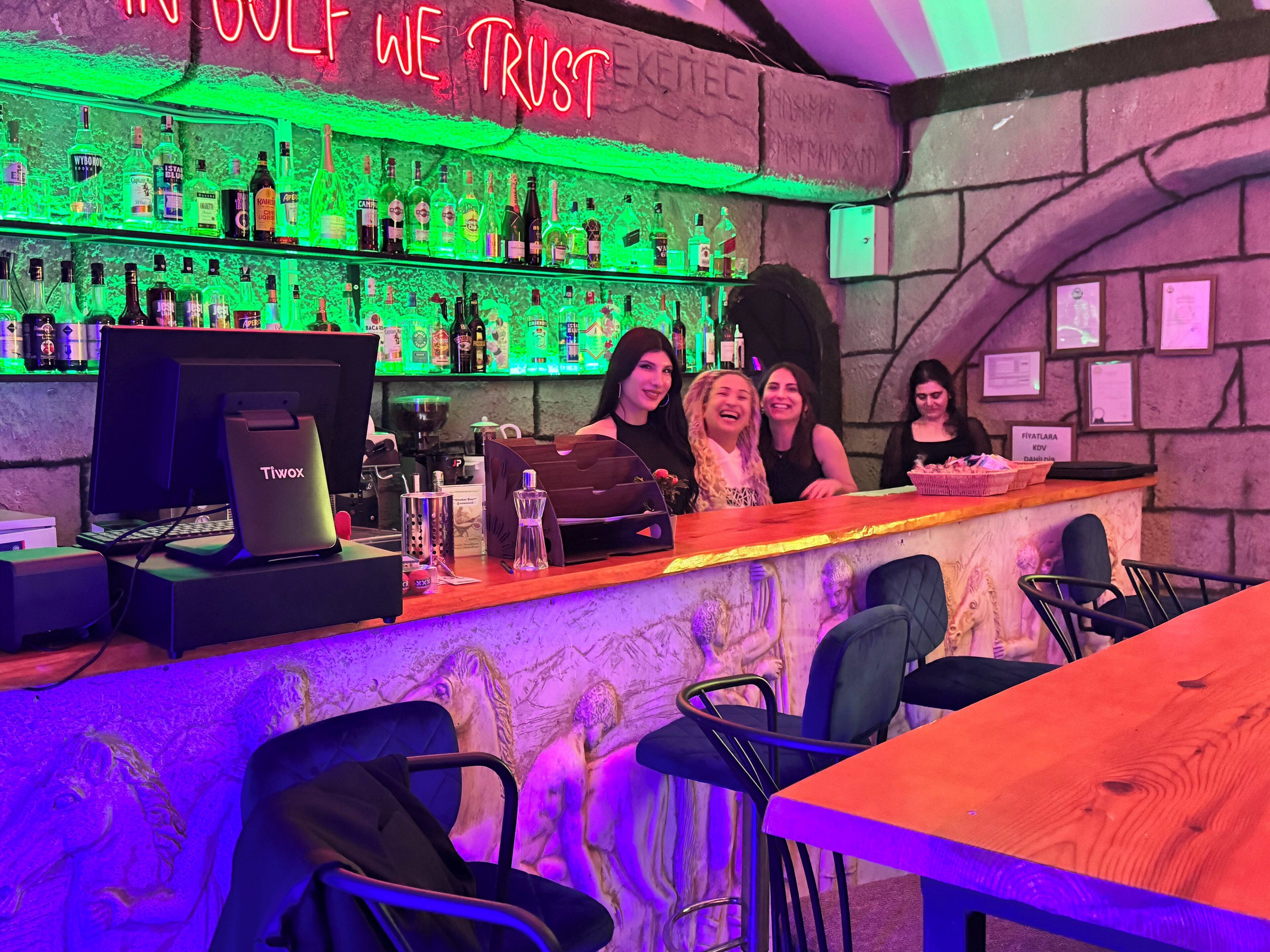 Un bar con un letrero de neón, una computadora y varias botellas.
