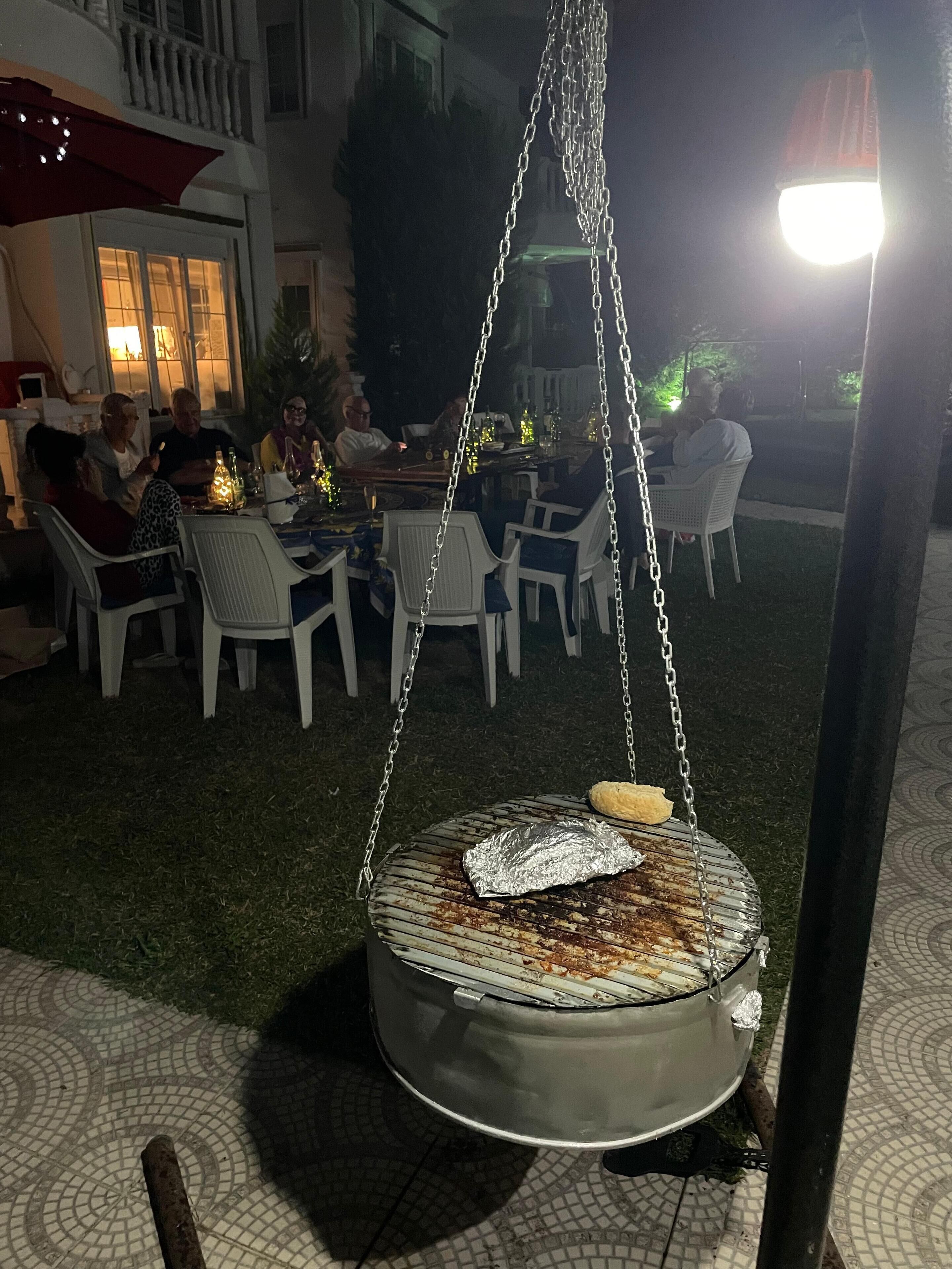 Un'area pranzo all'aperto con tavoli e sedie, una griglia pensile e un patio con pavimento piastrellato.