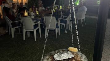 Un'area pranzo all'aperto con tavoli e sedie, una griglia pensile e un patio con pavimento piastrellato.
