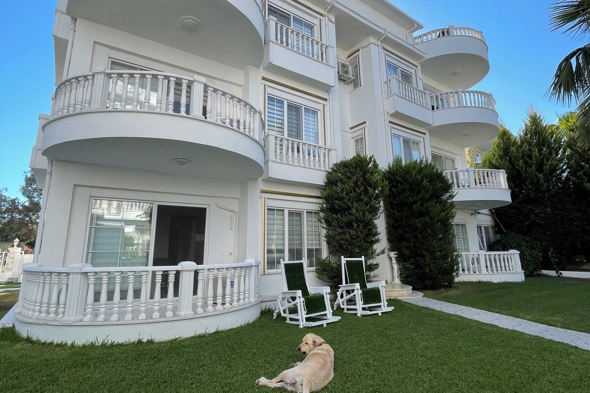 Un edificio de varios pisos con balcones, césped y un perro.