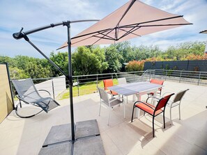 Une terrasse extérieure avec une table et des chaises, un grand parasol et une rambarde.