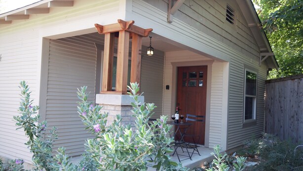 A house with a porch, a wooden pergola, and a table with chairs.